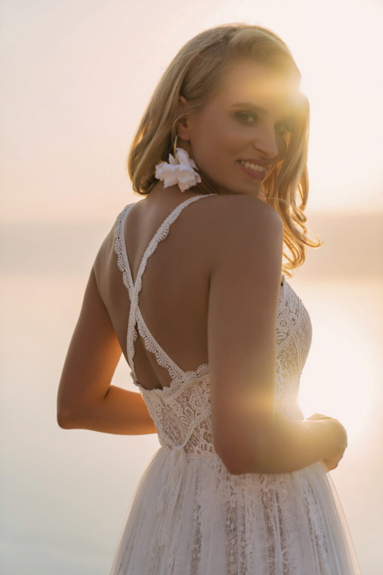Bjork Brautkleid von Dama Couture mit gekreuzten Spitzenträgern im Lingerie-Look – Brautmode, Braut im Gegenlicht am Strand