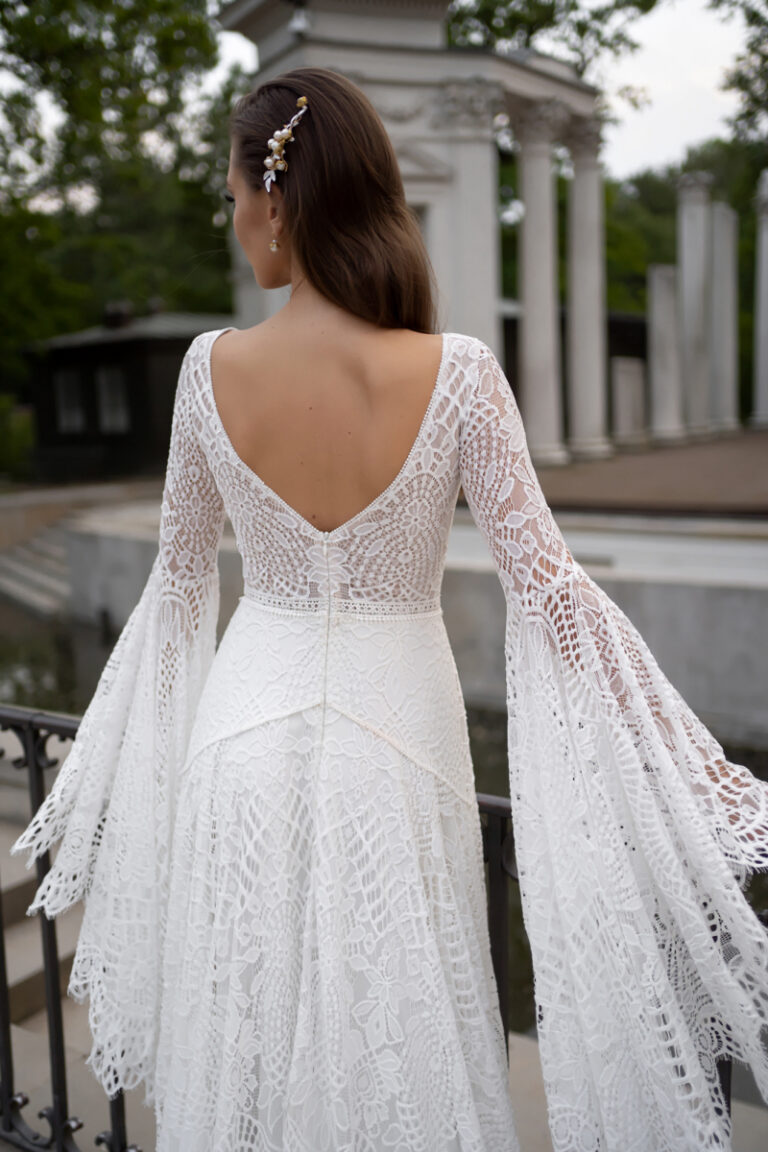 Boho-Brautkleid Lea von Dama Couture mit weiten Häkelspitzenärmeln und V-Rückenausschnitt – Brautmode, Rückenansicht im Park
