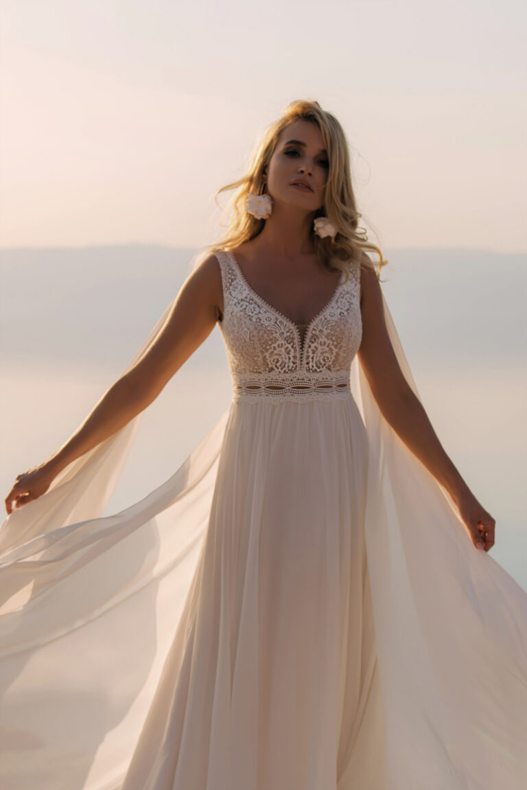 Brautkleid Atena von Dama Couture mit wehendem Cape und Spitzenoberteil – Brautmode, Braut am Wasser im Wind