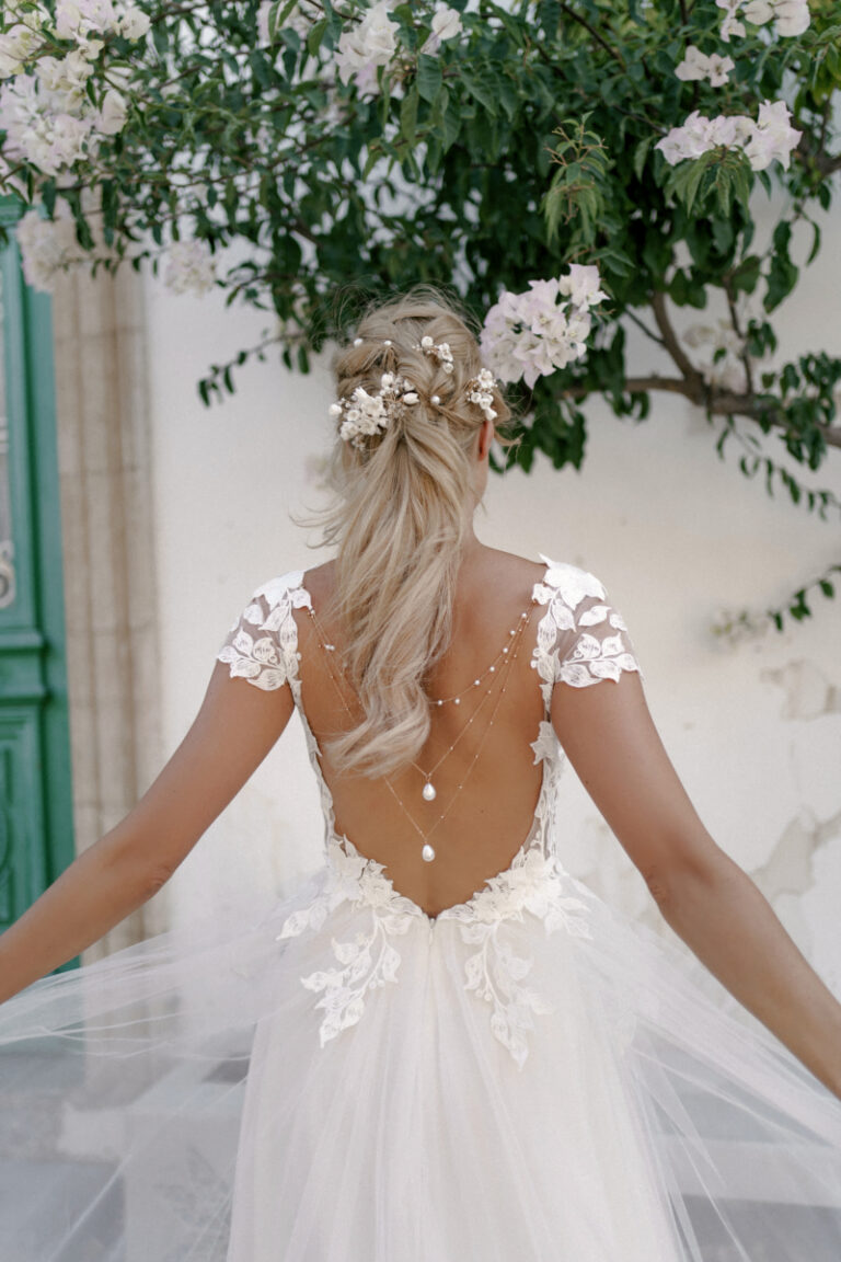 Brautkleid Lente von Dama Couture mit offenem Rücken, Perlenkette und Spitzenärmeln – Brautmode, Rückenansicht mit Blumenschmuck im Haar