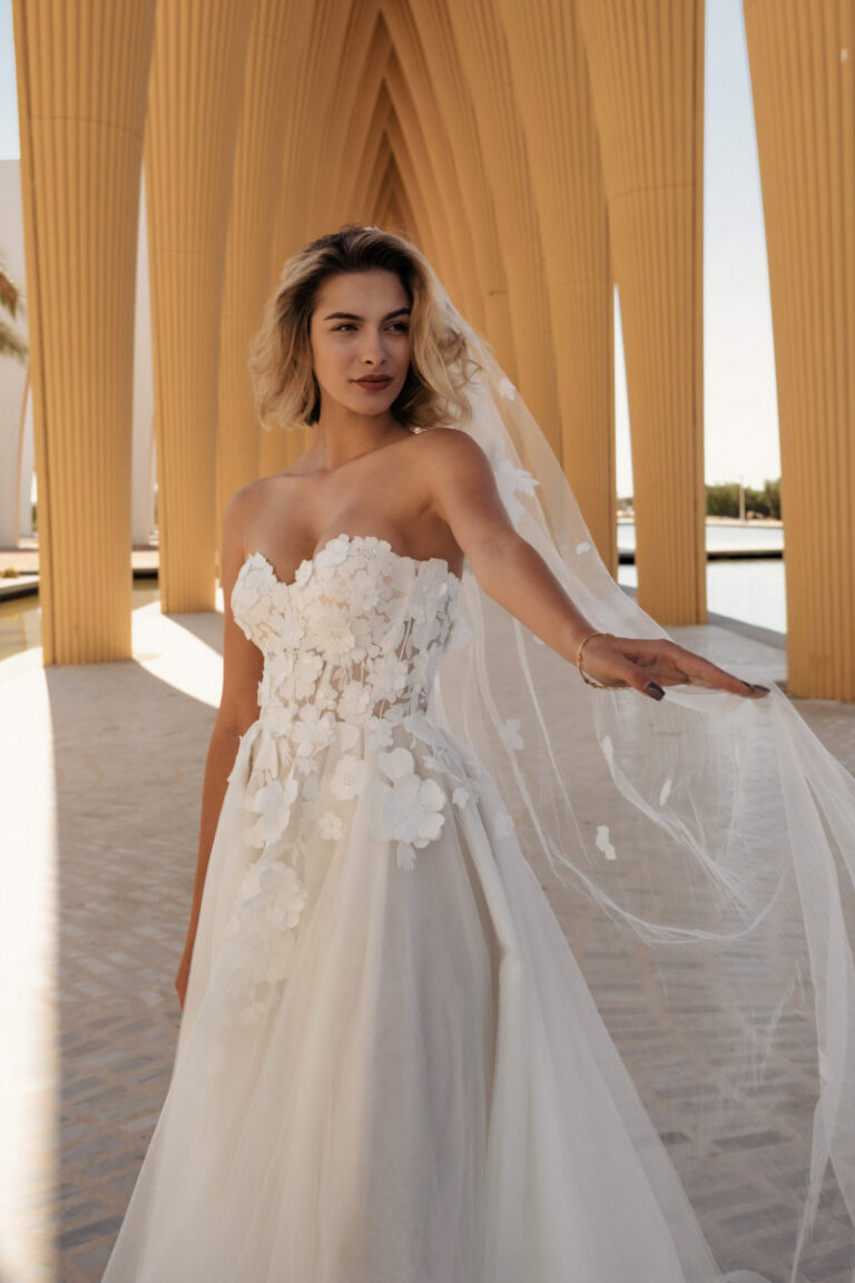 DAVINA Brautkleid mit Herzausschnitt und 3D-Blumenspitze – VeryNice Brautmode Lüneburg Winsen, Braut mit Schleier unter Bogengang