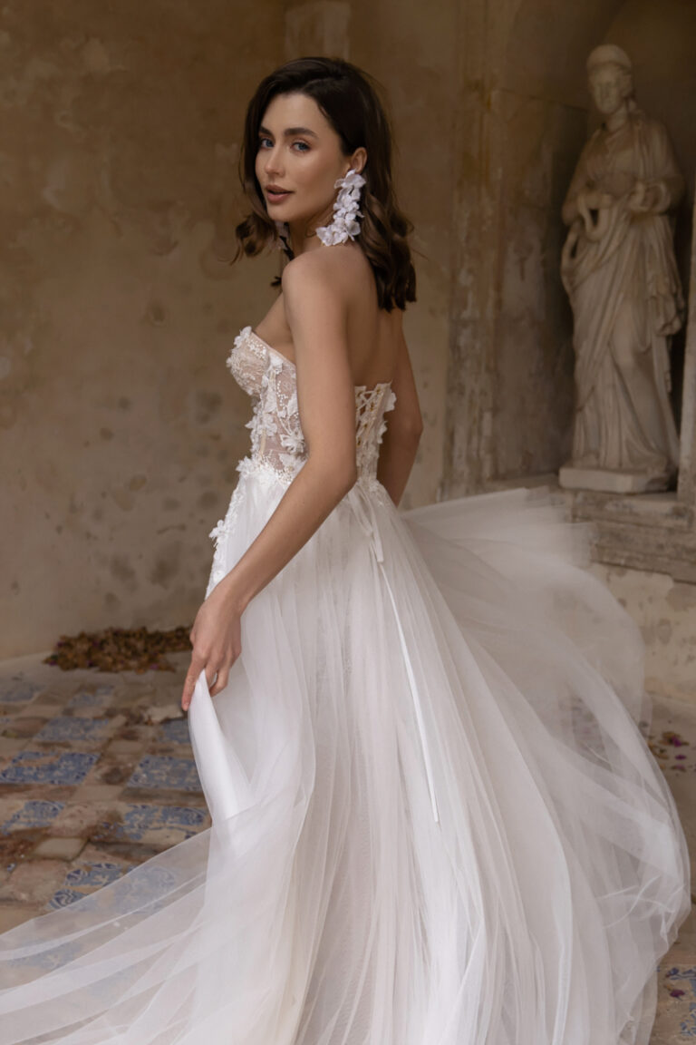 Kurzes Boho-Brautkleid Penelope von Dama Couture mit Korsage, Herzausschnitt und Tuellschleppe – Brautmode, Braut vor Steinstatue