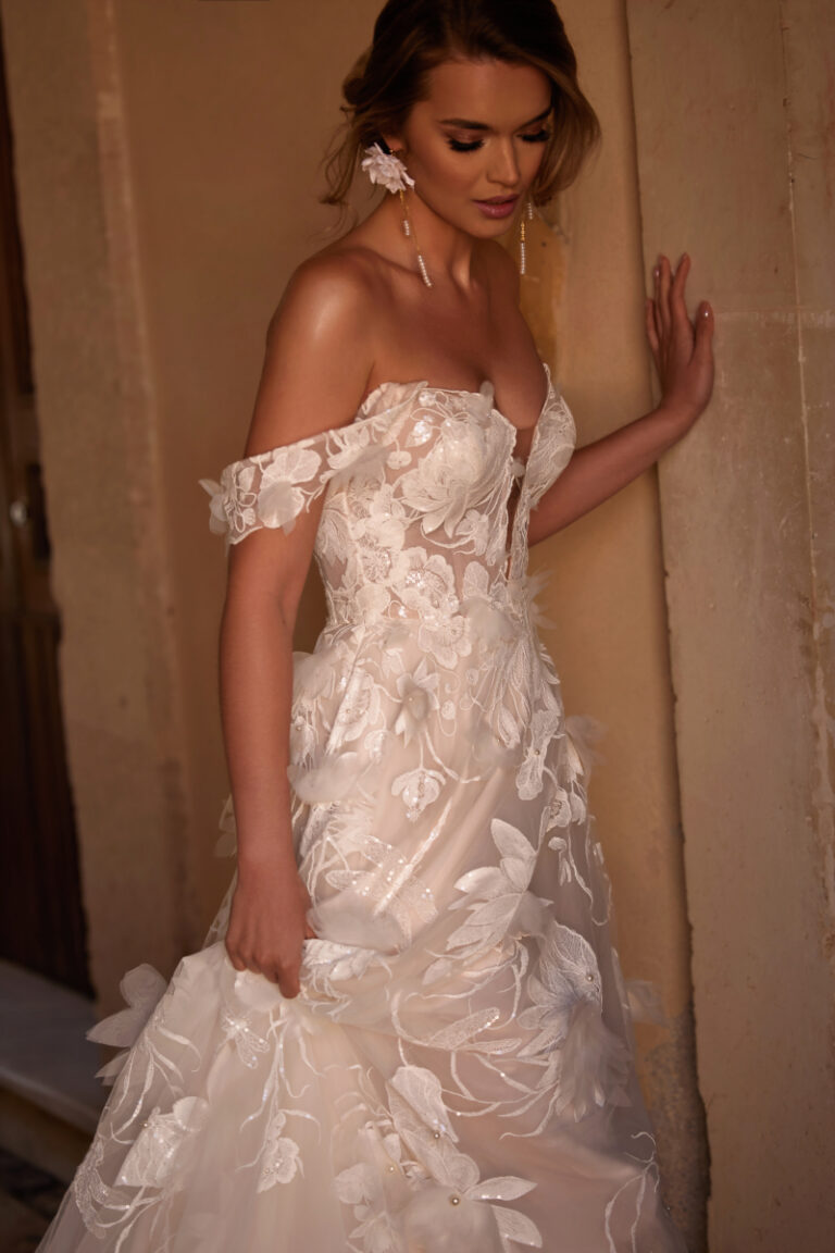 Nenufar Boho-Brautkleid mit 3D-Blumenspitze und Off-Shoulder-Ärmeln – Brautmode Hamburg, Modell im dramatischen Licht
